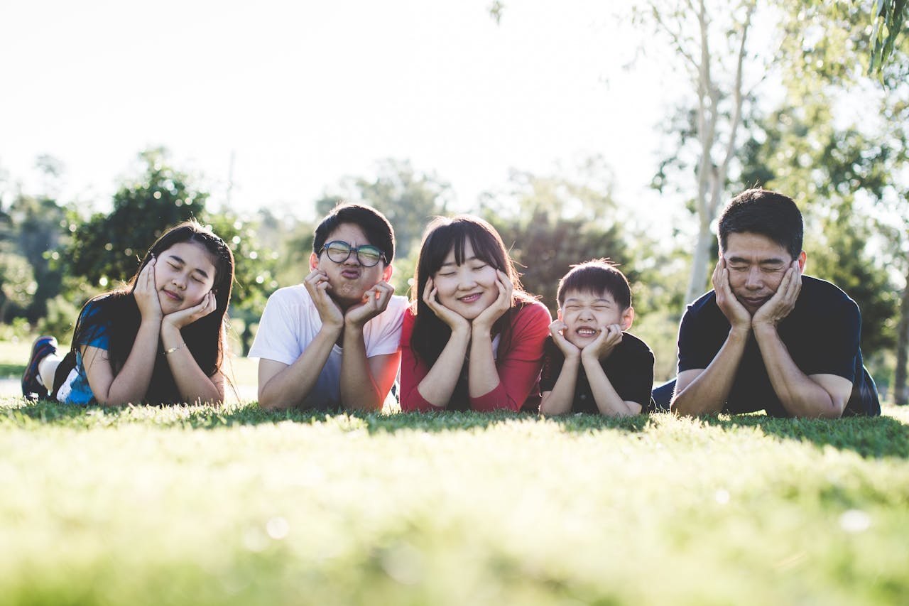 gallery-5 Asian family posing happily on the grass in a sunny park, showcasing love and togetherness.